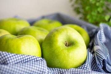 Green ripe apples on blue fabric on the white kitchen table.
