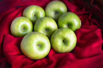 Green ripe apples on red fabric