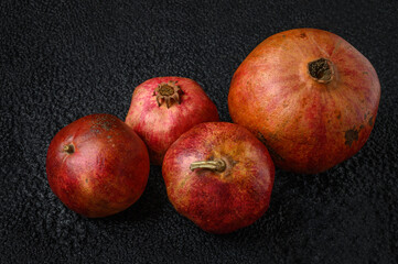 Fototapeta na wymiar One large ripe pomegranate fruit with three small pomegranate fruits on a dark background texture.