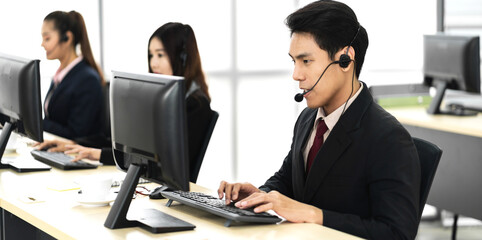 Group of happy asian smiling call center business operator customer support team phone services agen working and talking with headset on desktop computer at call center