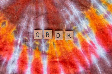 Grok spelled out in wooden letters on a hippie-style burst pattern tie dye textile background. February 2021. 