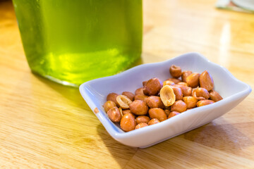 Salted fried peanuts in a plate near green beer on a table