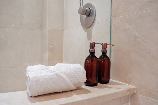 Amber glass shampoo bottles with copper steel pumps in a luxury marble hotel spa and shower.
