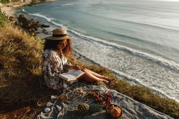 Portrait of a young brunette relaxing on the beach cliff, reading a book