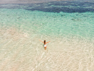 Fototapeta na wymiar Drone aerial view happy woman enjoying on beach with amazing clear turquoise water stand in the sea with open arms