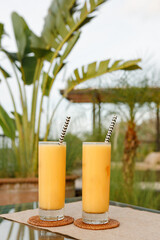 Two glasses of mango cocktail juice smoothie on the table in restaurant, summer tropical background