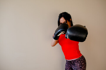 beautiful athletic girl with a fitness figure is holding boxing gloves after fighting against a beige background and sunbeams