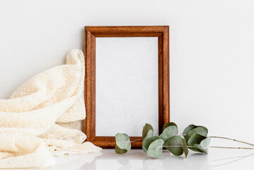 Wooden photo frame with a sprig of eucalyptus on a white wooden table. Minimalistic, delicate layout. Blank for a postcard.