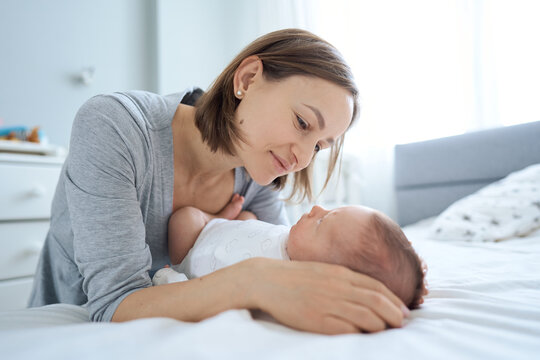 Close up of cute one months old baby boy lying on bed and playing with his Mum. Mum talking to son and cuddling him. High quality photo