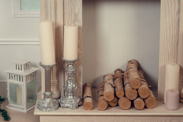 Antique white fireplace with wood in the studio. Nearby there are candles in candlesticks and a white glass box