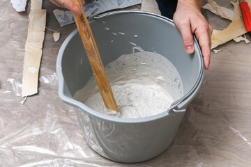 Mixing white plaster in a bucket with a stirrer. Close-up.
