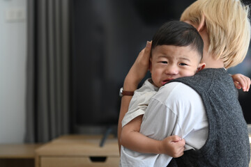 Image of Asian mother holding crying baby in comfortable home.