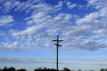 Obraz premium Power lines with blue sky and white clouds at sunset north of Hutchinson Kansas USA out in the country.