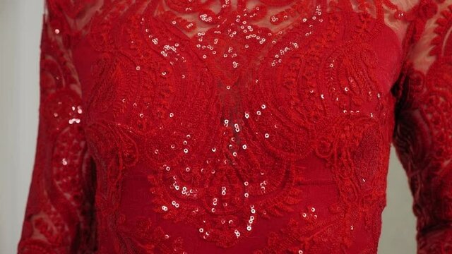 Close-up of a young woman in a red openwork evening dress in an atelier.