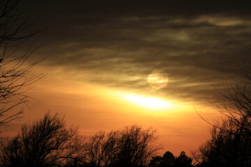sunset out in the country with the Sun coming threw the clouds with tree silhouette's north of Hutchinson Kansas USA .