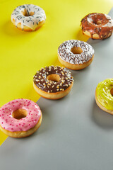 Multicolored donuts with glaze and sprinkles on a yellow-gray background