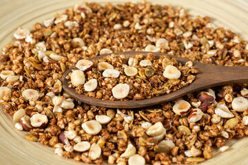 Homemade granola made from buckwheat. Organic buckwheat granola, green buckwheat sprouts, hazelnuts, pumpkin seeds, flax seeds and nutmeg. Granola in a wooden plate on a wooden table. Close-up