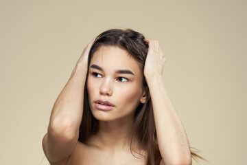 Fototapeta premium Brunette with bare shoulders close-up long hair beige background clean skin