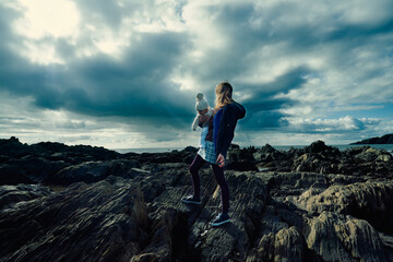 Young mother with baby in sling standing on the beach in autumn