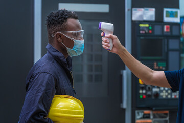 Industry workers used a medical Digital  temperature Thermometer to check staff body temperature before start work in factory ,they wearing face mask the concept of a corona virus [Covid-19] screening