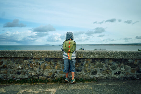 Preschooler looking over wall by the sea in autumn