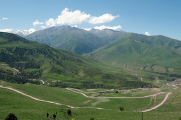 Fototapeta na wymiar The nature of Kyrgyzstan. Country road across mountains. Mountain landscape. Among green valleys, mountains are visible at middle of the day.