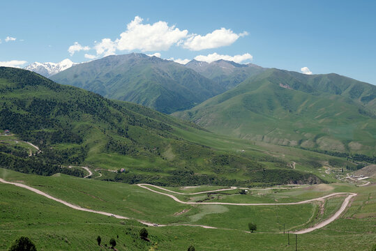 The nature of Kyrgyzstan. Country road across mountains. Mountain landscape. Among green valleys, mountains are visible at middle of the day.