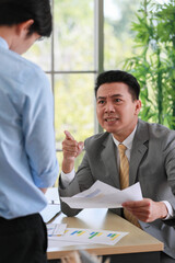 Asian businessman manager in suit holding paperwork and strong talking for young employee with anger and serious gesture look like he comments as disagree or unacceptable for his project work.