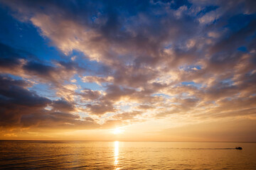 Calm sea with sunset sky and sun through the clouds over.