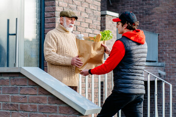 Food and good for seniors delivery online service. Delivery man carrying packages with ordered products. Happy old mature man receiving parcels. Social support for retirement.