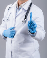 Male doctor in latex protective gloves points up with index finder on gray background. Unrecognizible medic in scrubs.