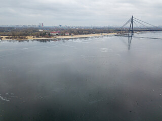 Obraz premium Reflection of the sky in thin ice on the Dnieper River in Kiev. Aerial drone view. Winter cloudy morning.
