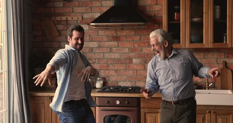 Overjoyed funky laughing young man dancing to disco music with happy energetic middle aged old father, making funny moves in kitchen, enjoying spending crazy weekend leisure time together at home.