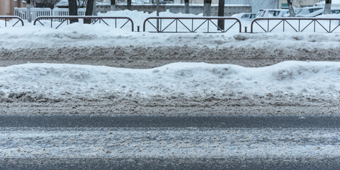 City paved road is covered with dirty stale snow during spring thaw.