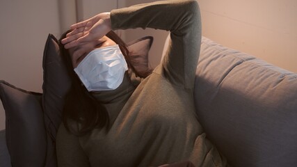 Young Asian woman suffering from coronavirus and uses mask blanket to keep warm