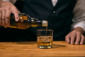 Waitress man standing pours whiskey into a glass 