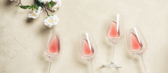Rose wine in glasses and decorative flowering sakura branch (artificial), banner. Beige concrete background. Top view, flat lay.