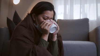 Sick Asian woman drinking lukewarm water and uses masks and blankets to warm