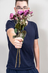 young guy in glasses with a bouquet of withered roses and shows FIG. unhappy love concept
