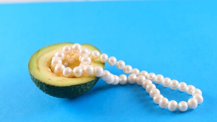 Half fresh avocado fruit with pearls on blue background. Fashionable food design.
