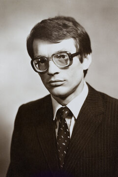 Portrait of young Soviet guy with glasses, in jacket and tie. Vintage black and white paper photo, 1970s. Transferred property, family archive. Outdated quality