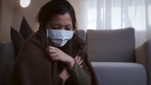 Young Asian woman drinking lukewarm water in times of suffering has chilling black eyelids all over her body due to a cold and uses masks and blankets to warm and quarantine herself