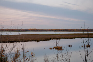 Sundown and sunrises. Blue sky with tints of purple and much clouds. Silhouettes of trees and grass are reflectioning in the river water. Background of heaven. Beautiful evening