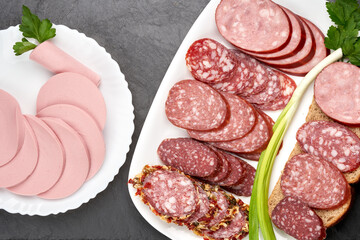Slices of different sausages on white plates, top view.