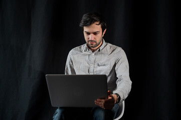 Pleasant positive business man using laptop.Happy smiling man in shirt works on laptop on a dark background