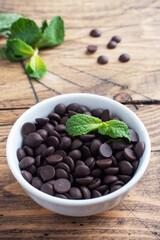 Chocolate drops for decorating desserts in a plate with mint on a wooden background.