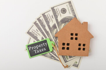 Top view of a house wooden and banknotes with written Property Taxes on white background. Selective focus.