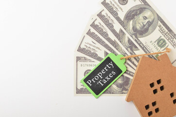 Top view of a house wooden and banknotes with written Property Taxes on white background. Selective focus.