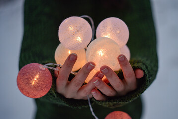 women's hands hold round burning balls of garland, the girl is dressed in a dark green sweater