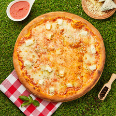 Delicious italian pizza quattro formaggi with the four cheeses Mozarella, Gorgonzola, Parmesan and Gouda on green grass background